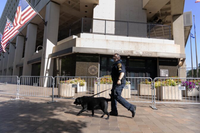 A Federal Bureau of Investigation police officer walks with his working dog outside Federal Bureau of Investigation building headquarters in Washington, Saturday, Aug. 13, 2022. (AP Photo/Jose Luis Magana)