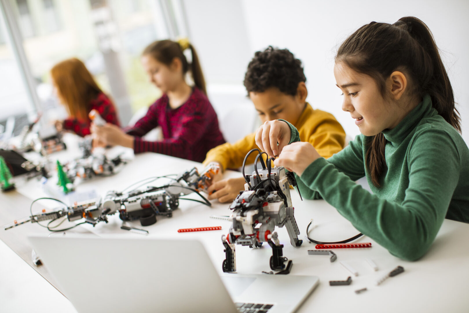 Group of happy kids programming electric toys and robots in robotics classroom