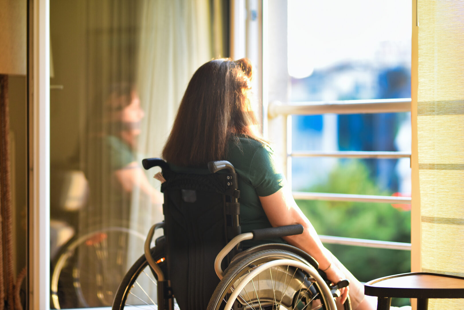 Woman in wheelchair in front of open window in her apartment