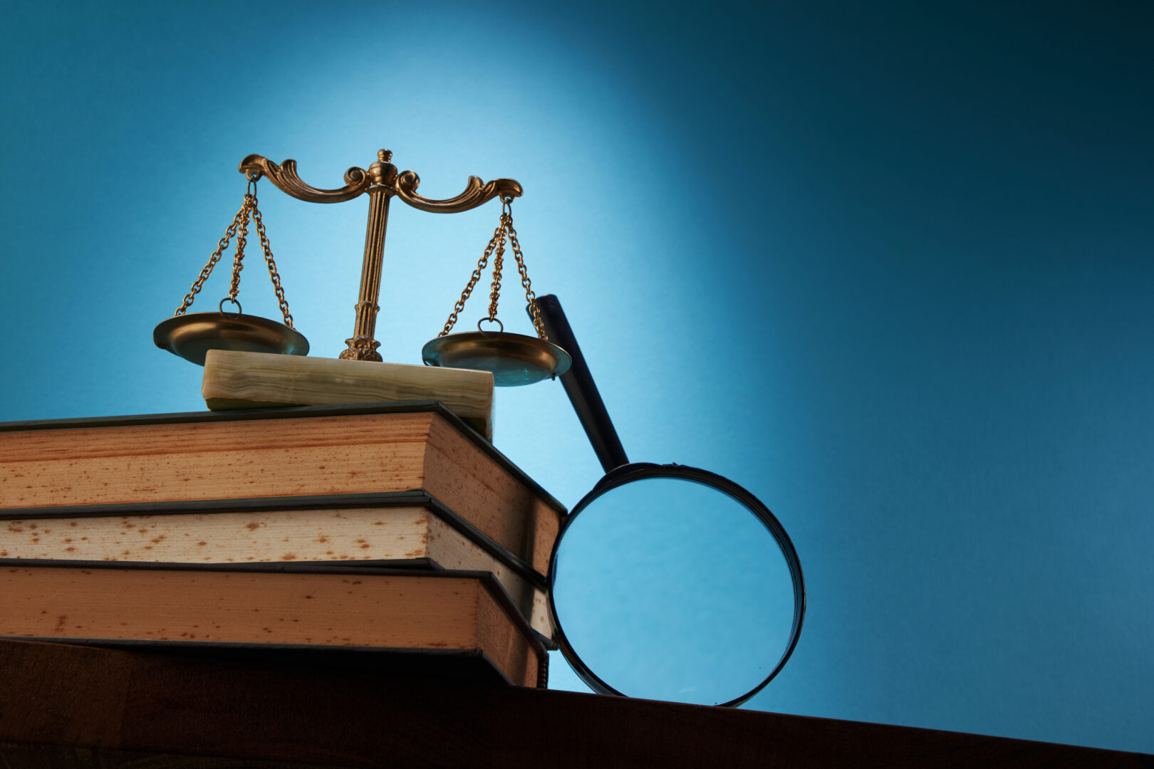 libra scale and magnifying glass on stack of books against blue background