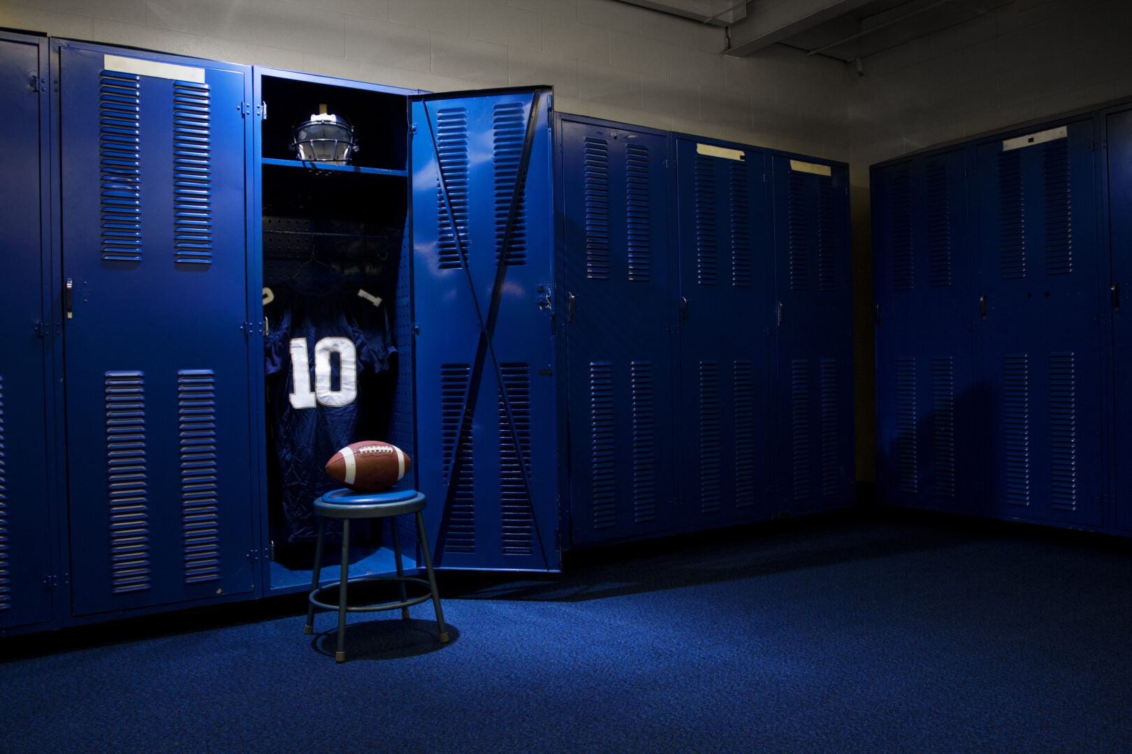 An open locker with a jersey, helmet and ball in a authentic football locker room