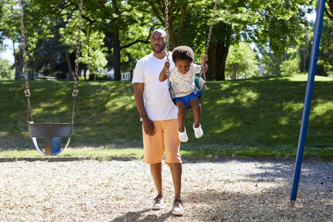 Royal Harris, pushes his grandson, Carter, 2, on swings at Woodlawn Park in Portland, Ore., Wednesday, July 20, 2022.