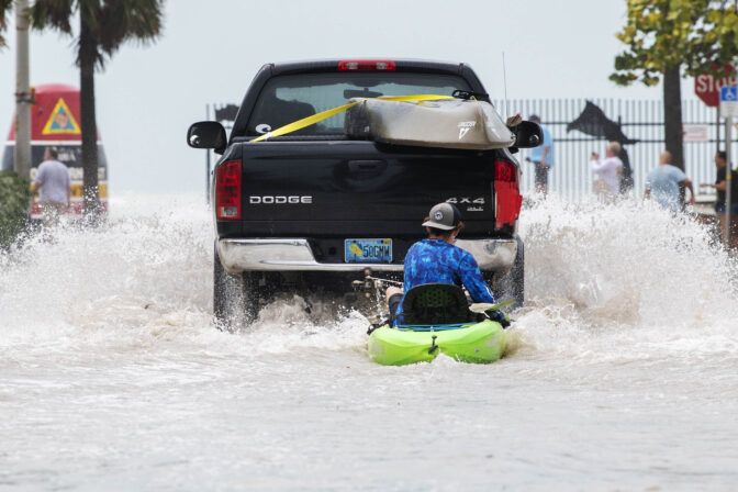 A truck pulls a man on a kayak on a low-lying road after flooding in the aftermath of Hurricane Ian