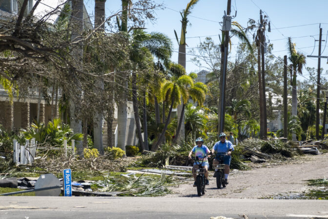 People ride bikes along a street in Punta Gorda Florida after hurricane Ian on September 30, 2022.