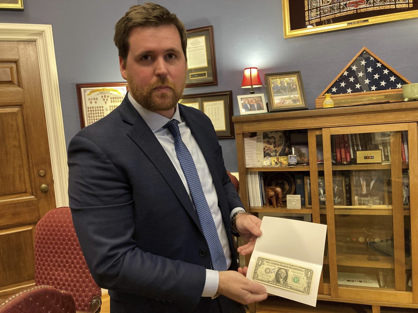Missouri Treasurer Scott Fitzpatrick displays a $1 bill signed by the former treasurer of the United States on Thursday, Dec. 15, 2022, at his Capitol office in Jefferson City, Mo. Due partly to rising interest rates, Missouri had earned more than $116 million on investments through the first five months of its current fiscal year — nearly double the amount earned the entire previous year.