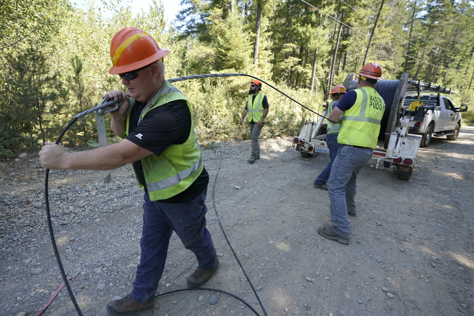 FILE - Carl Roath, left, a worker with the Mason County (Wash.) Public Utility District, pulls fiber optic cable off of a spool, as he works with a team to install broadband internet service to homes in a rural area surrounding Lake Christine near Belfair, Wash., on Aug. 4, 2021. Federal officials announced plans Thursday, July 28, 2022, to spend $401 million in grants and loans to expand the reach and improve the speed of internet for rural residents, tribes and businesses in 11 West and Central U.S. states. 