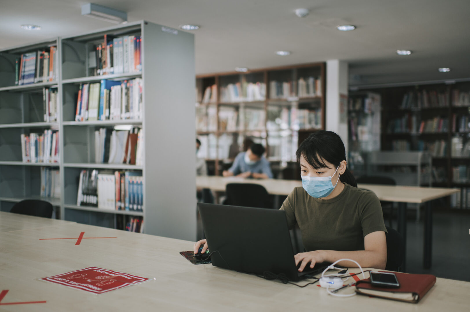 asian university student studying in library observing social distancing