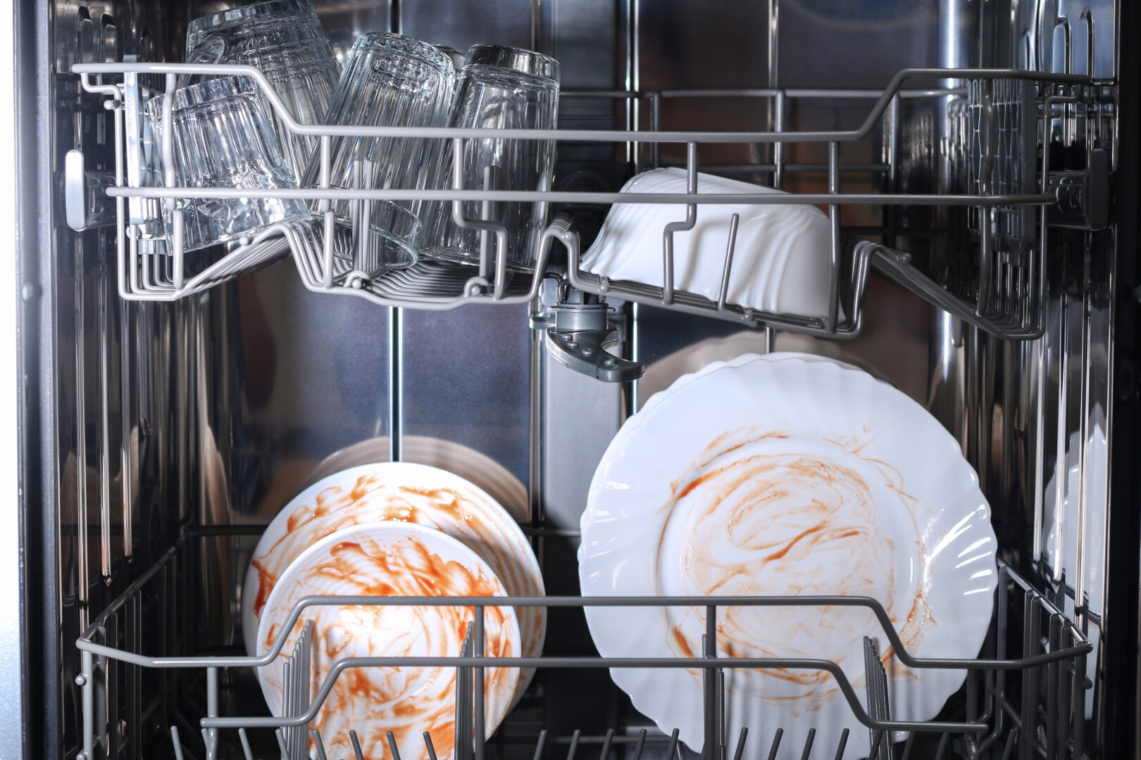 A man loads dirty dishes, plates, spoons, forks, cutlery into the dishwasher tray.
