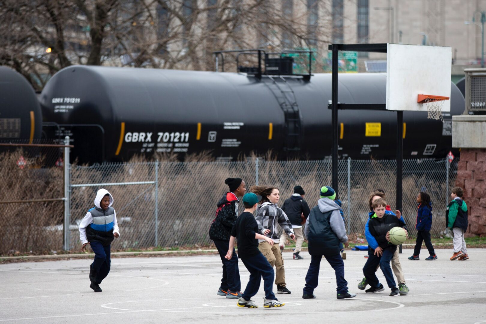 In this photo taken April 9, 2015, children play in view of train tank cars with placards indicating petroleum crude oil standing idle on the tracks, in Philadelphia. Rail tank cars that are used to transport most crude oil and many other flammable liquids will have to be built to stronger standards to reduce the risk of catastrophic train crash and fire under a series of new rules unveiled Friday by U.S. and Canadian transportation officials.