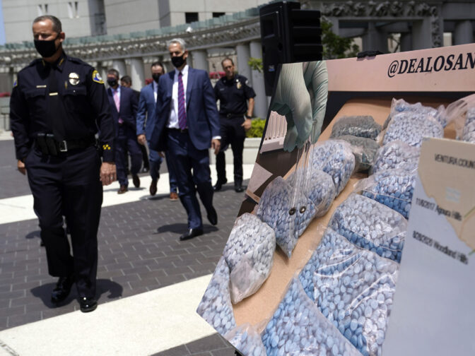 Officials walk past images of illegal drugs outside the Edward R. Roybal Federal Building on May 13, 2021, in Los Angeles. Authorities say a teenage girl died Tuesday night, Sept. 13, 2022, of an apparent overdose at a Los Angeles high school and police are investigating three other possible fentanyl overdoses in the area.