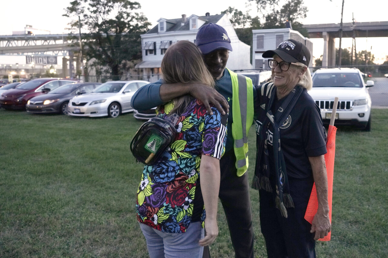 Reginald Rawls, center, greets two of his regular customers Amanda Harley, left, and Judy Harley at the Calvary Baptist Church parking lot which is located near the Philadelphia Union's Subaru Park, Wednesday, Oct. 4, 2023, in Chester, Pa. (AP Photo/Michael Perez)