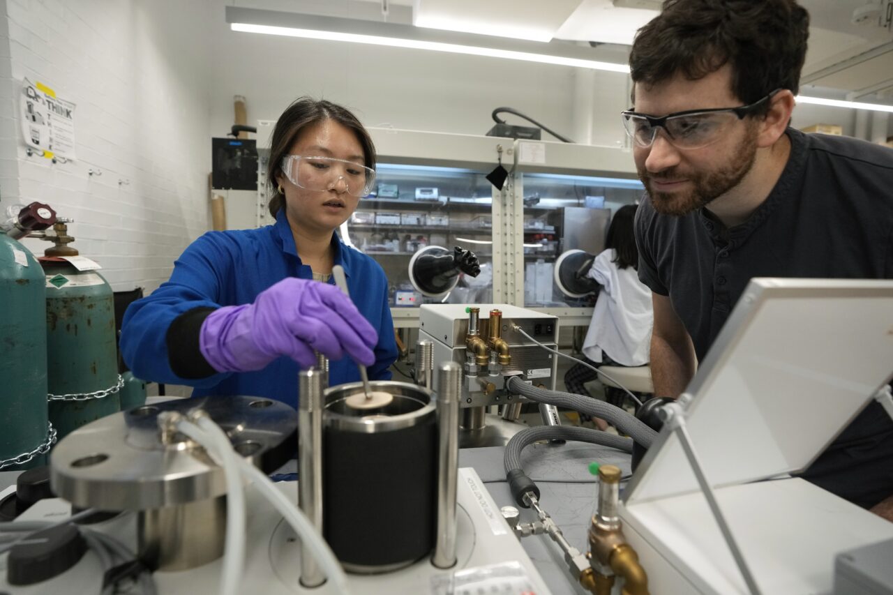 Harvard graduate student Faith Chen, of Wilmette, Ill., left, places a sample of cobalt-based hybrid material in a calorimeter, a device that measures temperature changes, as Jarad Mason, assistant professor of chemistry and chemical biology at Harvard University, of Watertown, Mass., right, looks on, Thursday, Sept. 14, 2023, in a lab on the school's campus, in Cambridge, Mass. The experiment is part of research to develop a more environmentally-friendly solid refrigerant that could be used as an alternative to existing volatile refrigerants. (AP Photo/Steven Senne)