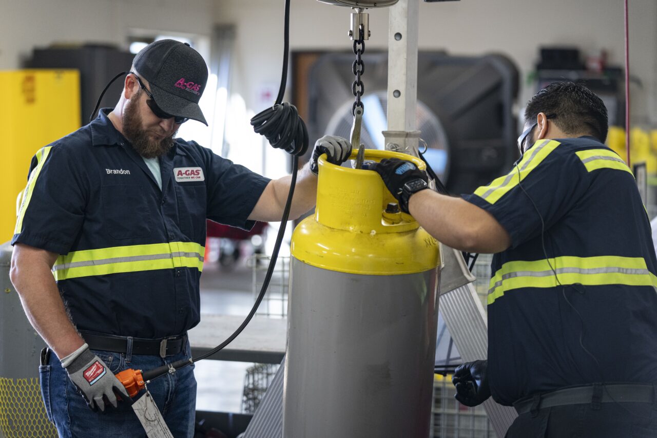 Operators use a hoist to move a used refrigerant cylinder at the A-Gas Rapid Recovery DFW facility on Monday, Oct. 9, 2023, in Arlington, Texas. The company takes in shipments of refrigerators and tanks from around the country and beyond, drains them, then purifies and reclaims the chemicals, shipping out recycled product. This prevents the need for new chemical production. (AP Photo/Sam Hodde)