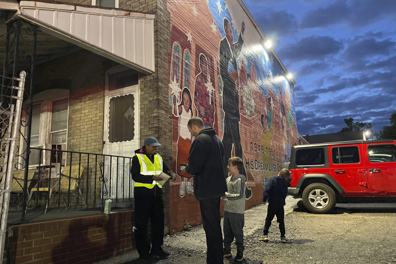 Philadelphia Union soccer fan Abe Gitterman, center, with his children, pays Calvary Baptist Church member Lisa Lewis, left, a fee for parking at the church lot in Chester, Pa., on Saturday, Oct. 7, 2023, in front of a mural that pays homage to Martin Luther King Jr., who attended the church as seminarian. The church, near Philadelphia Union's Subaru Park, has transformed its parking lot into game-day fundraisers for charities, ministries and a new speaker system that will allow Calvary to broadcast its services online. (AP Photo/Luis Andres Henao)