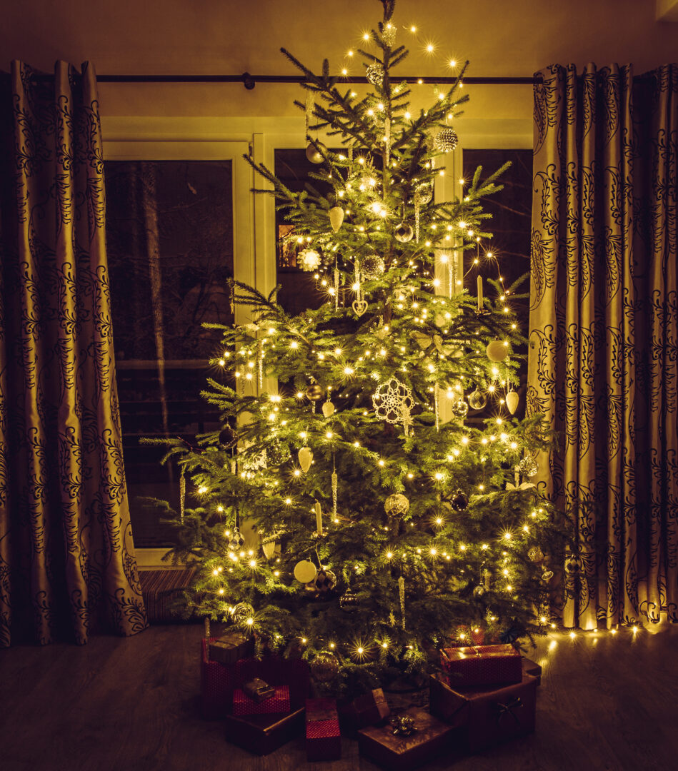 Christmas tree with warm yellow string lights and white icicles and snowflake shape ornaments. Red packed presents under the tree.