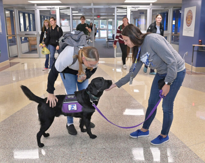 Elizabethtown Area High School student Morgan Johns pets Murphy, 4, the school's facility dog, as his owner, school counselor Amy Robinson, stands at the entrance of the school on Friday, Oct. 13, 2023.