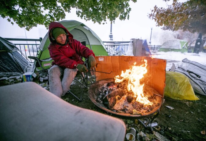 A man named Arturo, who came to Denver after leaving his home in Venezuela, tends to a fire by his tent, which is set up across the street from a Zuni Street hotel where he was staying, until he had to leave. Oct. 28, 2023.
