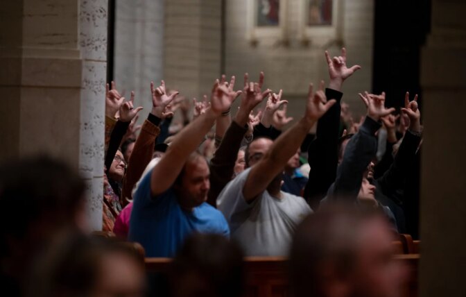 At the OneLewiston Community Vigil, attendees sign “I love you” as Kevin Bohlin, a member of the deaf community, delivers remarks in American Sign Language in the Basilica of Saints Peter and Paul in Lewiston, Maine, on Sunday, Oct. 29, 2023. (Raquel C. Zaldívar/New England News Collaborative)