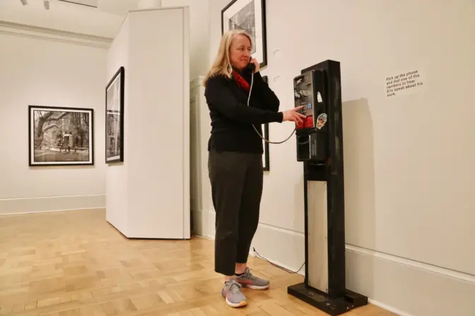 Curator Jeanne Bracy uses one of two payphones in ”Life-Lines Throughout the United States,” an exhibit at the Maguire Museum at Saint Joseph’s University. Through them, visitors can hear the artist, Eric Kunsman, talking about his work, or hear from people who still rely on the antiquated technology. (Emma Lee/WHYY)