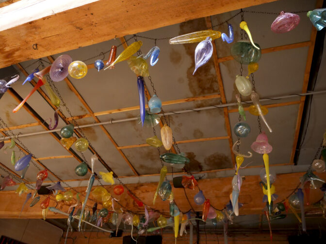 Blown glass hangs from the ceiling of the Juice Box Public House on March 6, 2024. The dark spots on the ceiling show where the roof was leaking and threatening the business. (Jeremy Long - WITF)