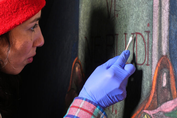 Art conservator Naomi Ruiz uses a cotton swab on a mural by Maxo Vanka that depicts the hand of God handing a tablet to Moses, inside St. Nicholas Croatian Catholic Church in Millvale, Pa., Wednesday, Feb. 19, 2025. (AP Photo/Gene J. Puskar)