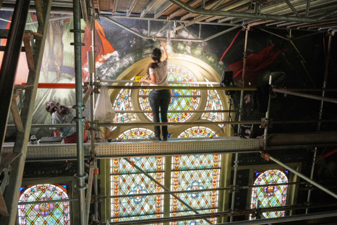 Standing on a 32-foot-tall scaffold, conservation technician Celeste Parrendo works on touching up a mural by Maxo Vanka inside St. Nicholas Croatian Catholic Church in Millvale, Pa., Monday, May 19, 2025. (AP Photo/Gene J. Puskar)