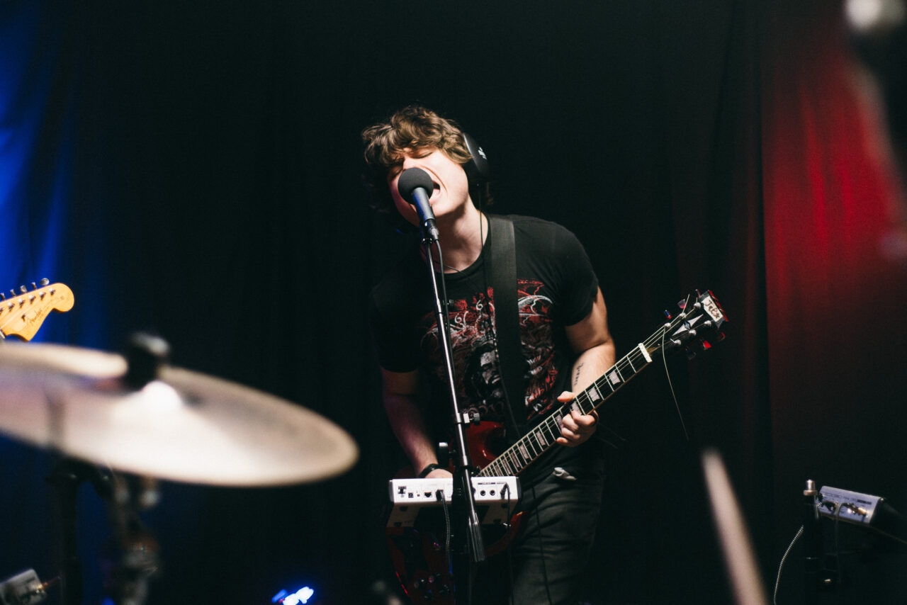 A singer shouting into a microphone and playing guitar