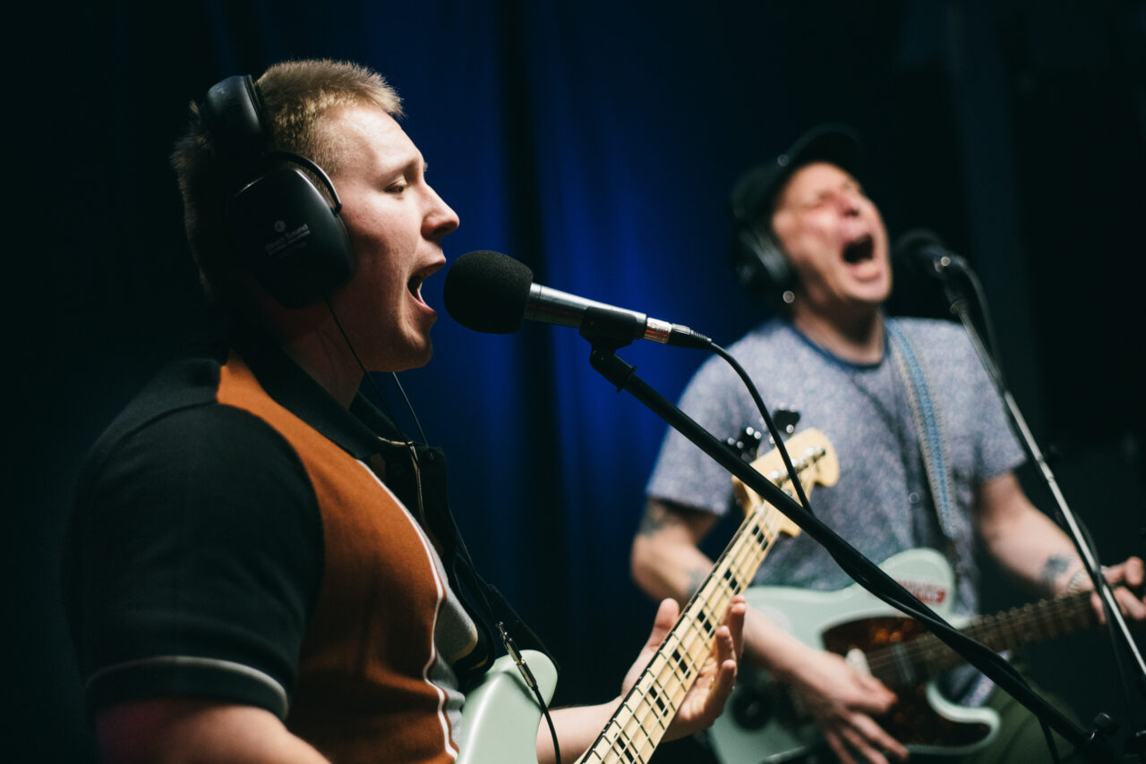 Two guitarists singing into microphones